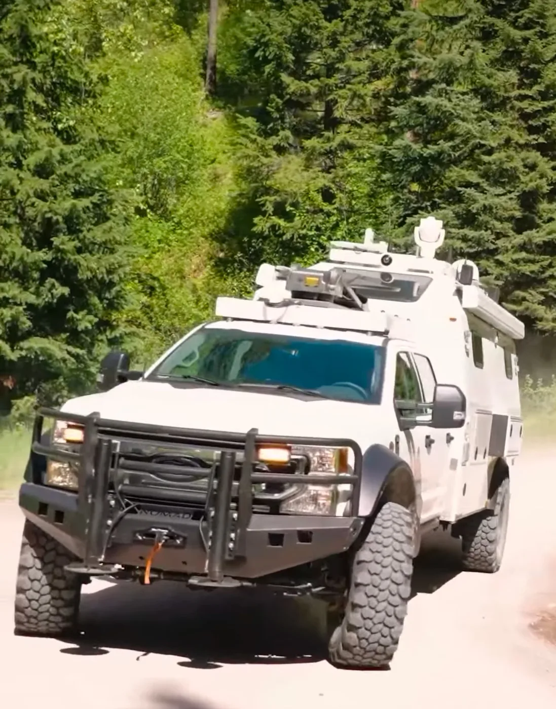 White armored command vehicle on DBL super single wheels running a forest road