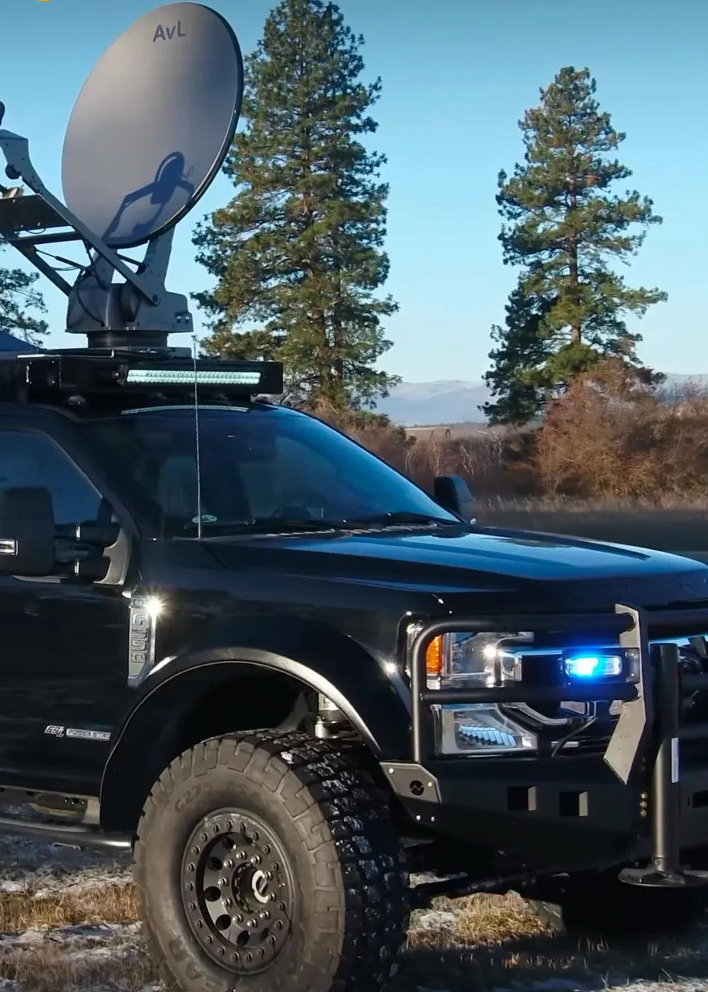 Black Super Duty with a roof-mounted AvL satellite antenna, grille guard and blue emergency lighting