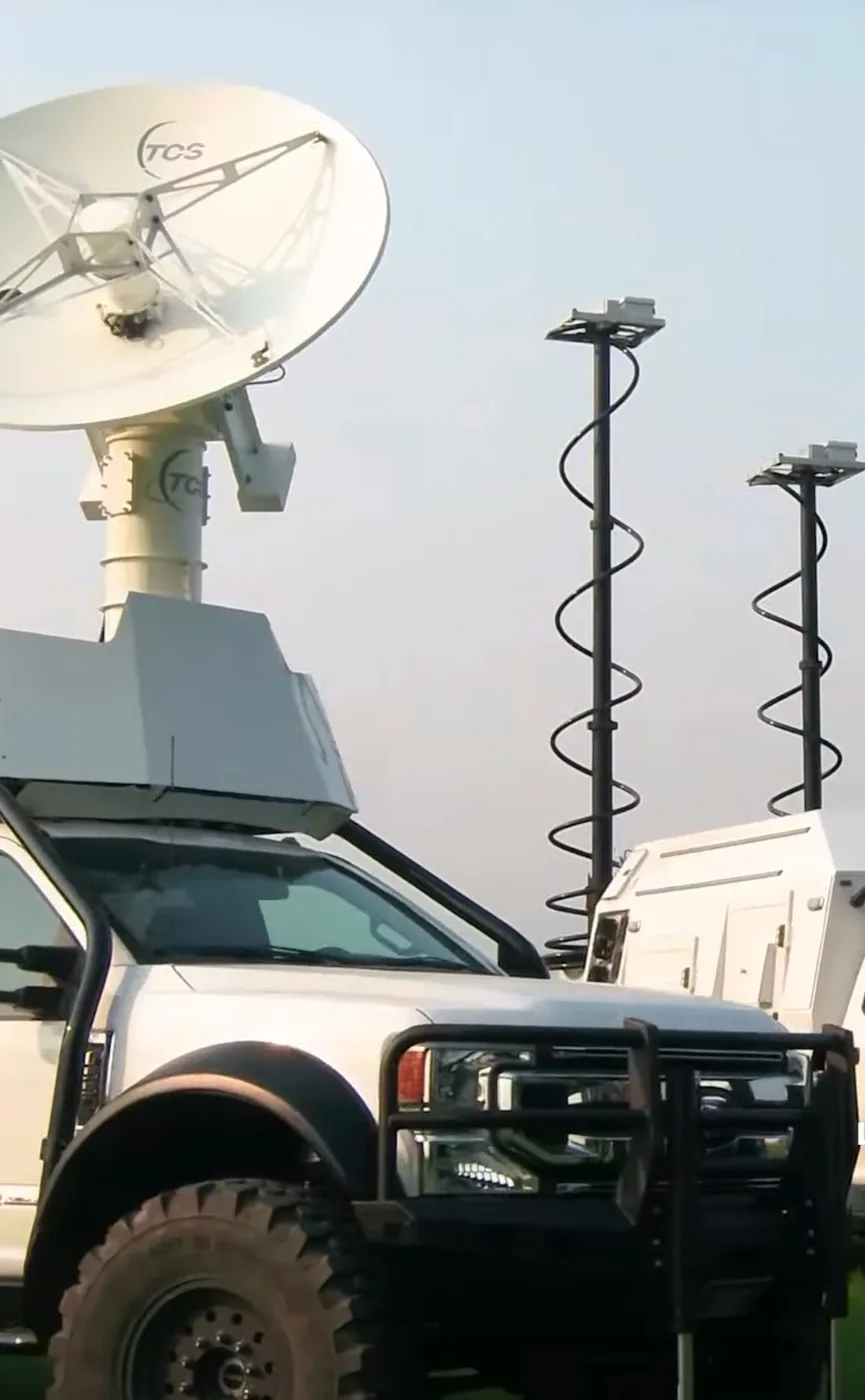 White communications truck with a TCS satellite dish and telescoping light masts deployed